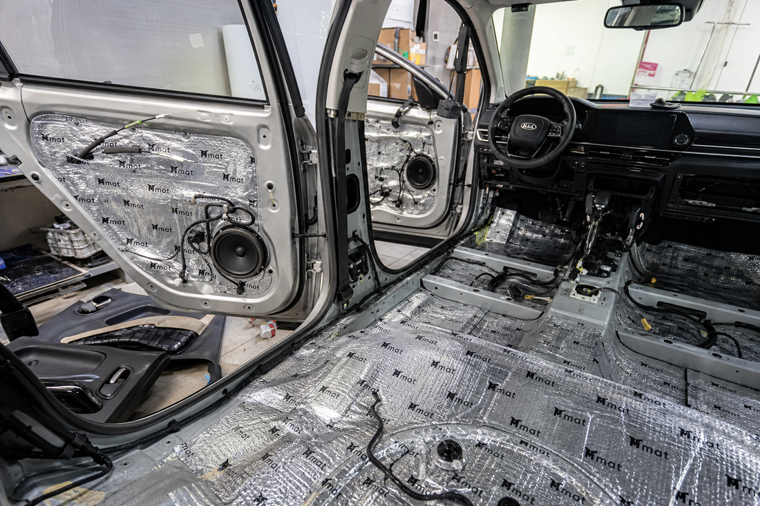 Butyl sound damping sheets installed on a car door, floor, and wheel arch with trim panels removed.